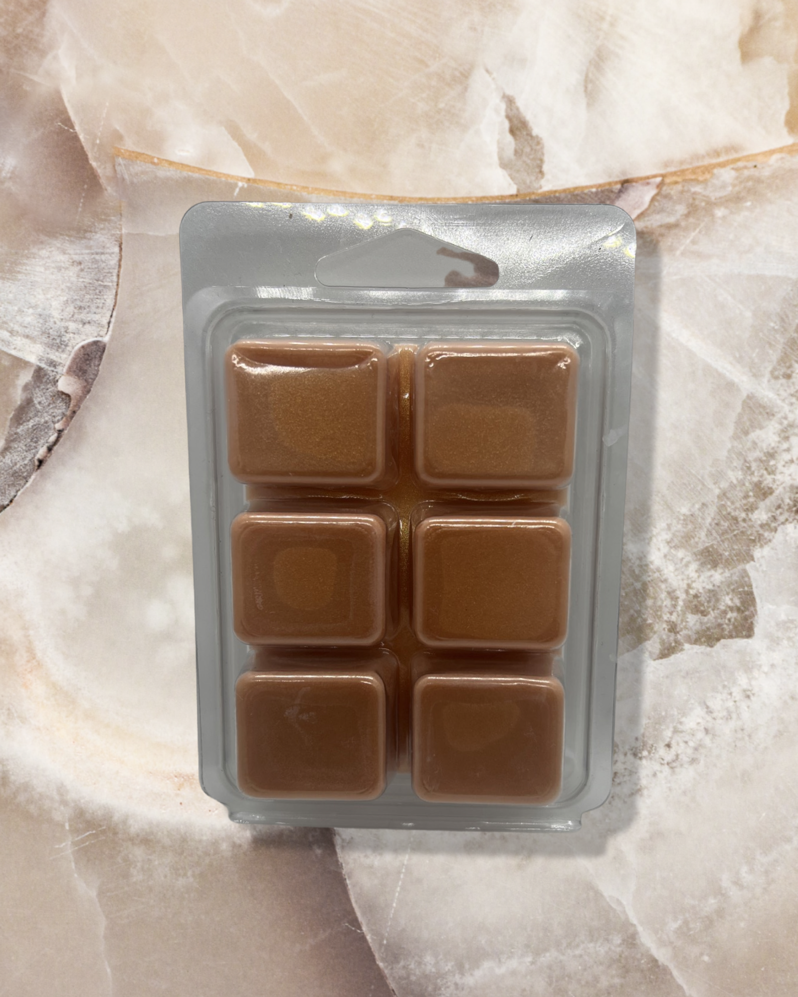 Apple Spice wax melts in a clear plastic clamshell package featuring six brown-colored cubes arranged in a symmetrical grid, displayed on a light marble surface with warm ambient lighting.