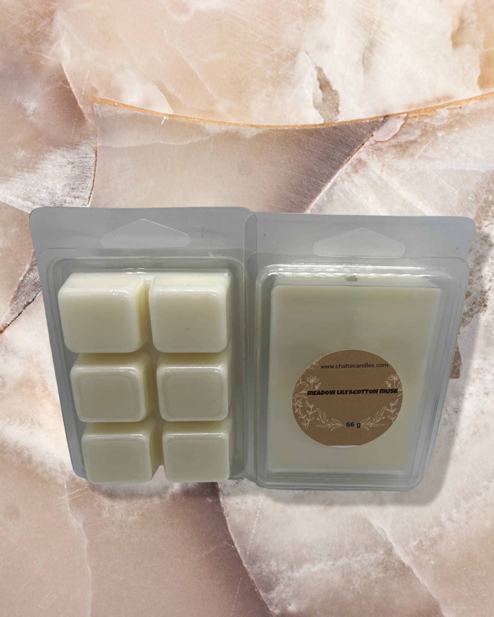 Meadow lily&cotton musk scented wax melts in creamy white color, presented in two clear plastic clamshell containers against a textured beige background. Features 6-cube segmented tray and single bar format with elegant round product label. By Mijn winkel