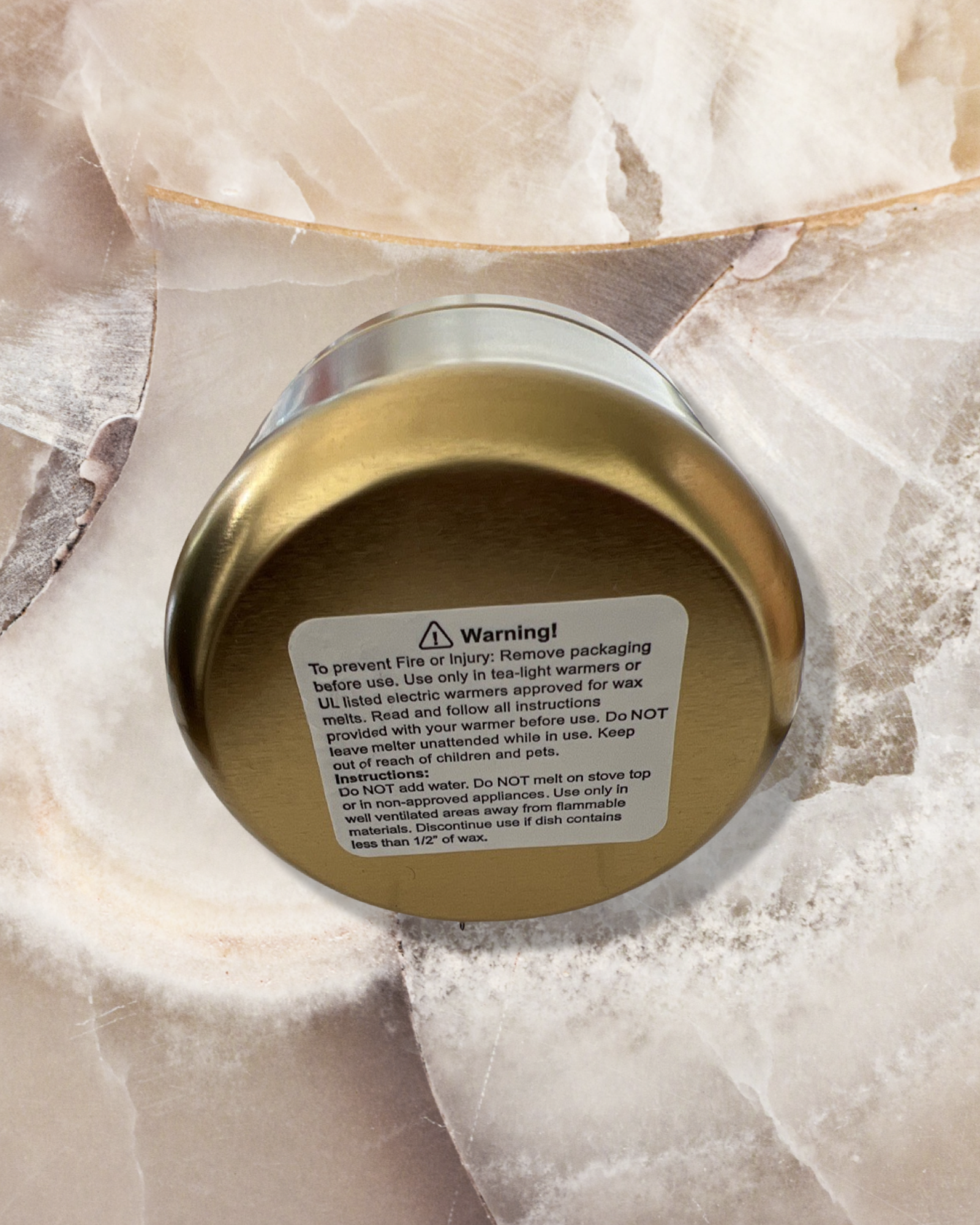 Chatte Peppermint candle in a golden metallic tin container with safety warning label, photographed on textured white marble surface, showcasing premium home fragrance product with professional product warning information