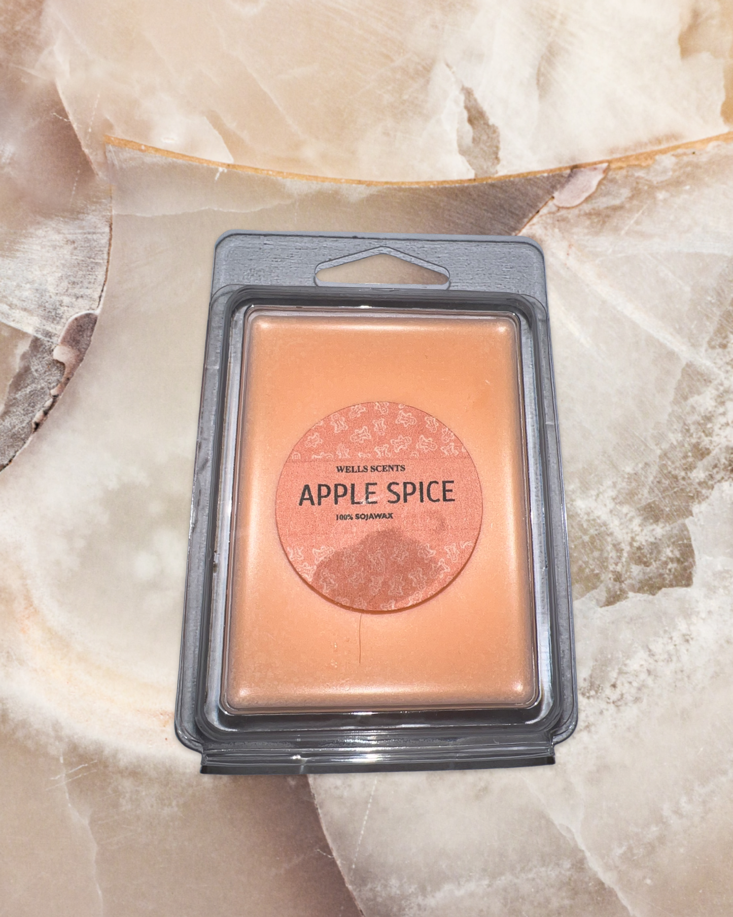 Apple Spice wax melt in peach-colored rectangular package with gray plastic clamshell container, featuring circular label design on textured marble surface background