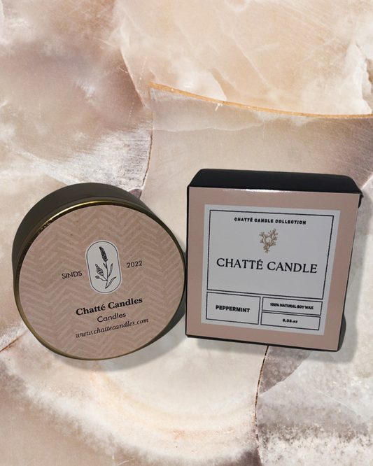 Chatte Peppermint candle displayed in elegant packaging featuring a round metal tin with botanical design and matching square box in soft rose gold tones, photographed on a luxurious marble surface with natural lighting highlighting the premium product presentation