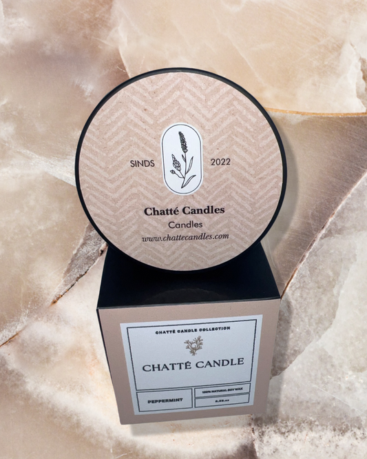 Chatte Peppermint candle packaging featuring a circular lid with botanical logo and chevron pattern, sitting on a beige square box with minimalist labeling, photographed on a textured cream-colored surface with natural lighting