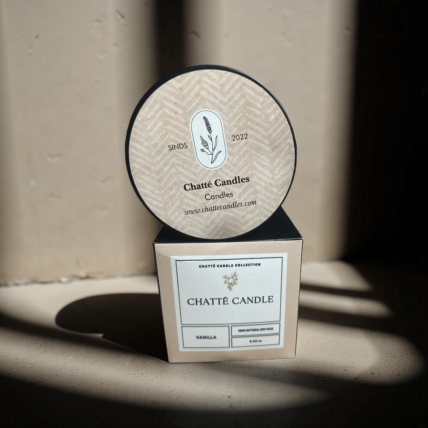 Vanilla candle in beige and black minimal packaging with botanical logo by Chatté Candles, established 2022, on sunlit surface